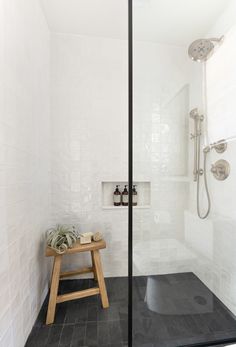 a walk in shower sitting next to a wooden stool on top of a tiled floor