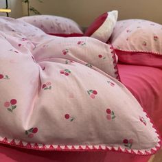 two pink pillows with cherries on them are sitting on the edge of a bed