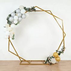 a white and gold balloon arch with greenery, balloons and garland on the sides