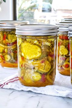 four jars filled with pickled vegetables sitting on top of a white table cloth next to a window