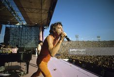 a man in an orange outfit singing into a microphone on top of a stage at a concert