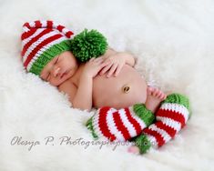 a newborn baby wearing a green and red striped hat with pom - poms