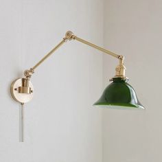 a green light hanging from the side of a white wall next to a gold lamp