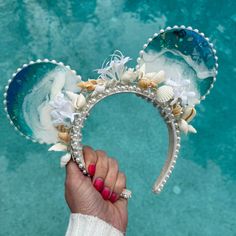 a hand holding up a mickey ears headband with seashells and pearls on it