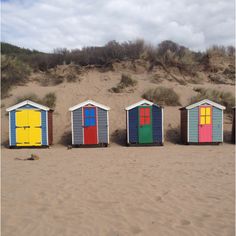 four beach huts painted in different colors on the sand