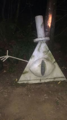 a white triangle with an eye on it in the middle of a dirt road at night