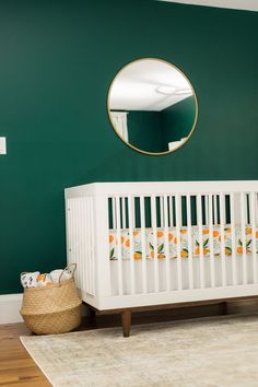 a white crib in front of a green wall with a round mirror above it