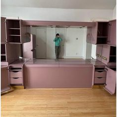 a woman taking a selfie in the mirror of a room with pink cabinets and drawers