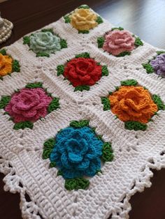 a crocheted blanket with multicolored flowers on it sitting on a wooden floor