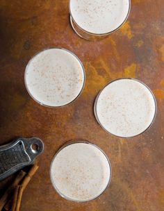 three glasses filled with white liquid sitting on top of a table next to cinnamon sticks