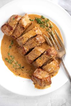 a white plate topped with meat covered in gravy and garnished with parsley