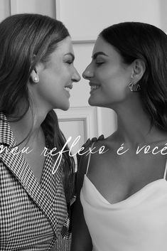 two beautiful women standing next to each other in front of a white wall with words