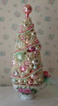 a decorated christmas tree sitting on top of a white bowl with pink and green ornaments