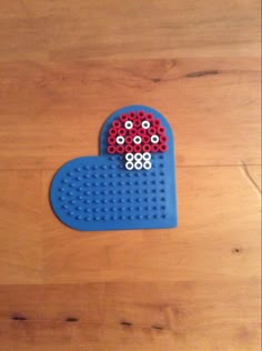 a heart shaped object made out of legos on a wooden floor with red and blue beads