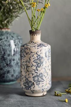 a blue and white vase with yellow flowers in it sitting on a table next to other vases