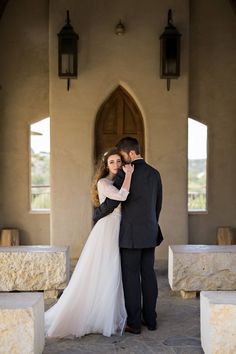 a bride and groom standing in front of a church doorway with their arms around each other