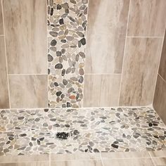 a walk in shower sitting next to a white tiled wall and floor with pebbles on it