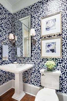 a white toilet sitting under a bathroom mirror next to a sink in a room with blue and white wallpaper