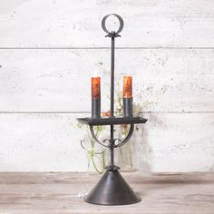 an iron candle holder with two candles in it on top of a wooden table next to a white wall