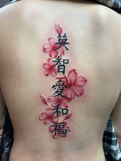 the back of a woman's lower back tattoo with flowers and chinese characters on it