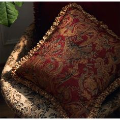 a red and gold pillow sitting on top of a chair next to a green plant