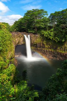 a large waterfall with a rainbow in the middle of it and trees on both sides