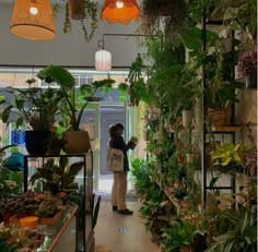 a woman is looking at plants in a store with lights hanging from the ceiling above her