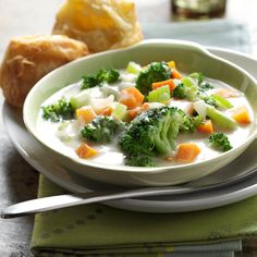 a bowl of soup with broccoli, carrots and bread on the side