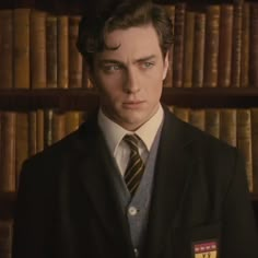 a man in a suit and tie standing in front of a book shelf with books on it