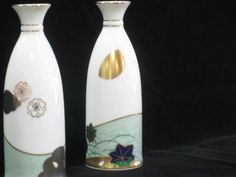 two white vases sitting next to each other on a black surface with gold accents