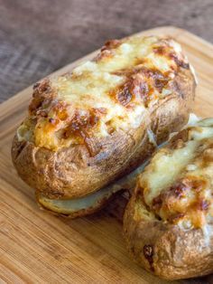 two baked potatoes sitting on top of a wooden cutting board with cheese and meat in them