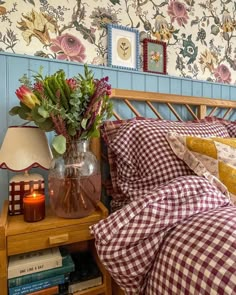 a vase with flowers on a nightstand next to a bed in a room that has floral wallpaper