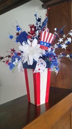 a red, white and blue flower arrangement in a patriotic vase on a wooden shelf