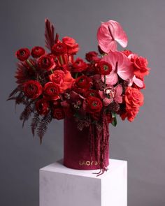 a red vase filled with flowers on top of a white pedestal