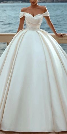 a woman in a white wedding dress standing on a balcony near the water with her hands on her hips