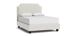 a white bed with two pillows on top of it and a night stand underneath the headboard