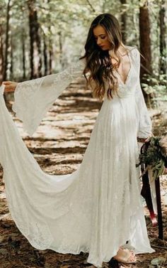 a woman in a white dress is walking through the woods with her long sleeves open