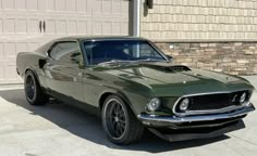 a green muscle car parked in front of a garage