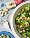 a bowl filled with broccoli and cheese next to other food on a table