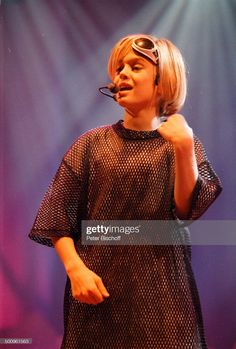 a woman with sunglasses on her head standing in front of a microphone and wearing a black dress