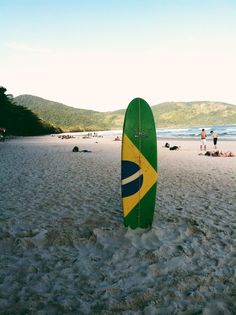 a green and yellow surfboard sticking out of the sand on a beach with people in the background