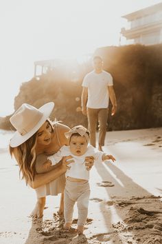 a woman holding a baby in her arms while standing on the beach with other people