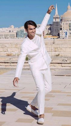 a man in white suit and sunglasses is dancing on the ground with his hand up