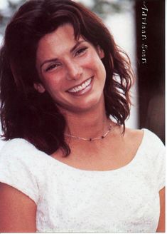 a woman smiling and wearing a white top with her hair in a half up style