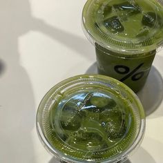 two cups filled with green liquid sitting on top of a white table next to each other