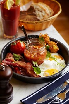 a plate with eggs, bacon, tomatoes and other food on it next to a drink