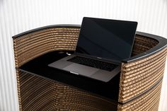 an open laptop computer sitting on top of a wicker chair next to a white wall