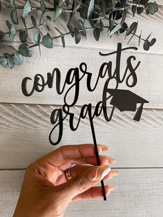 a hand holding a graduation cake topper with the words congrats grad on it