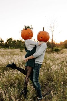 two people are hugging in a field with pumpkins on their heads