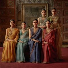 four women in sari sitting next to each other on a red carpeted floor